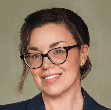 Headshot of Anne Corbin, woman with glasses and hair in an updo.