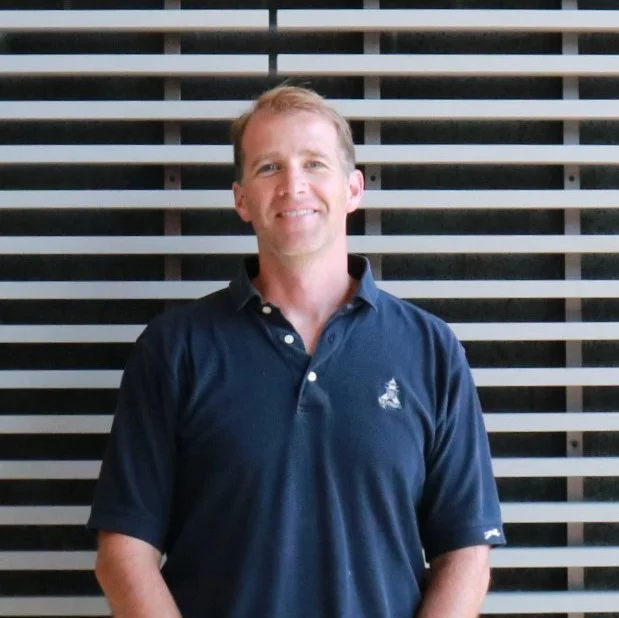 Portrait of Brian Wysor, man standing against wall with blue shirt.