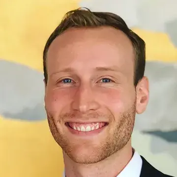 Jacob Bueno de Mesquita, portrait of man smiling with yellow backdrop.
