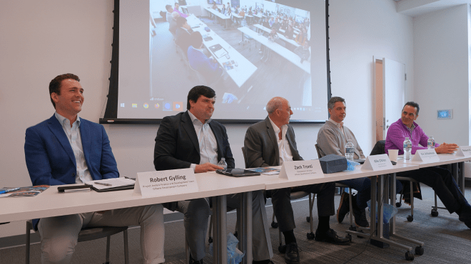 The five real-estate panelist sitting in the front of the room smiling.
