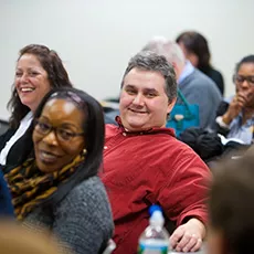 A male student smiling in a packed classroom.