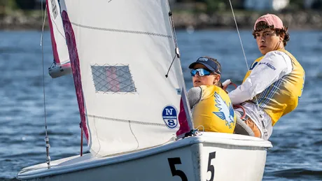 Two students navigate a small sailboat during sailing practice.