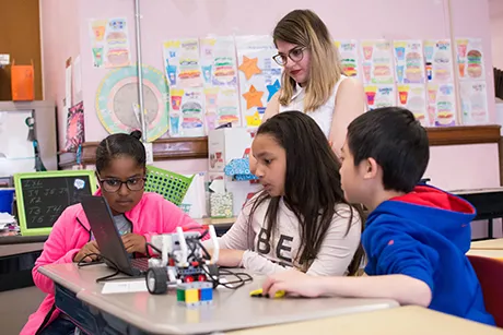 RWU student teacher watches as four students work on a laptop