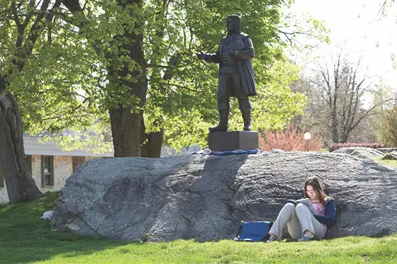 image of student reading on grass in front of Roger statue on RWU's Bristol campus