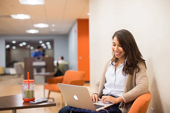 A person sits looking down on a laptop and smiling