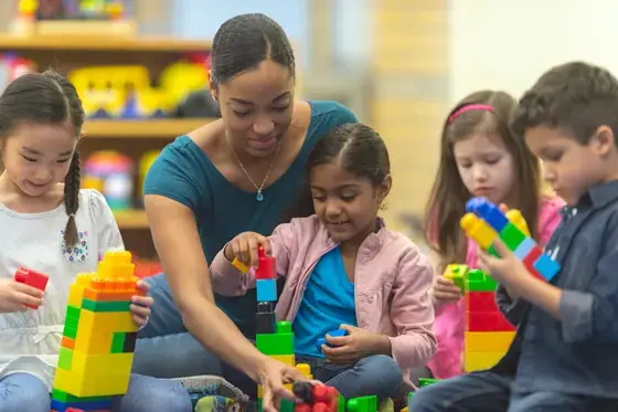 A teacher sits with schoolchildren building with blocks