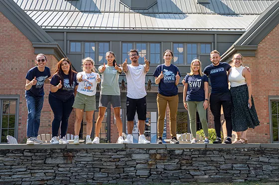 A group of students stand on a stone wall on RWU's Bristol Campus
