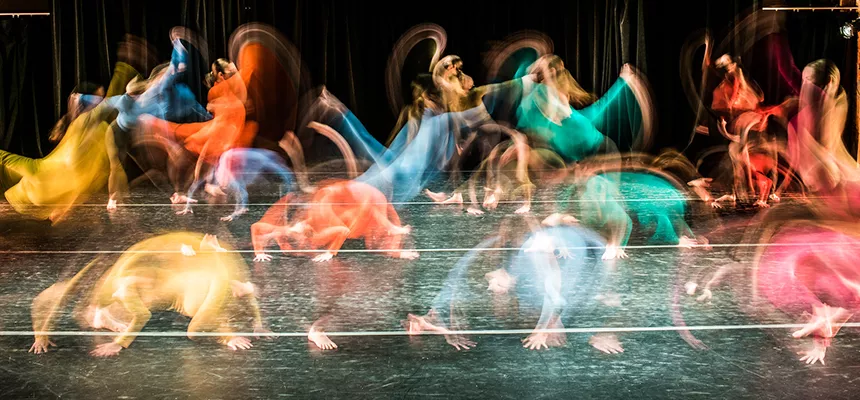 Dancers in colorful costumes make a rainbow with their bodies