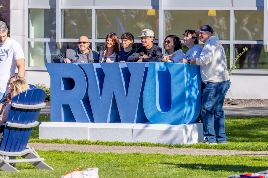 A family gathers to take a photo with giant RWU block letters.