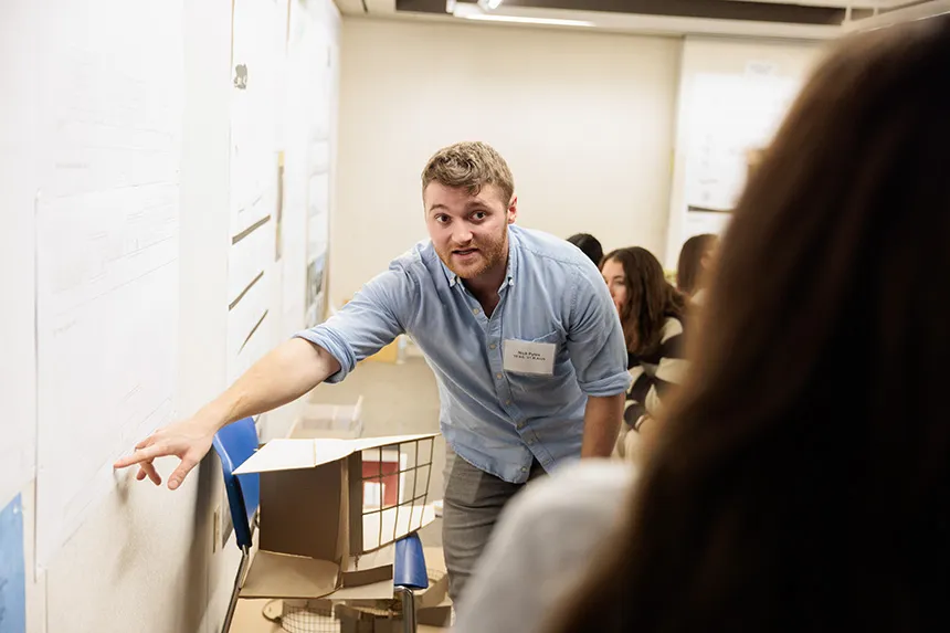 An Architecture alum points at a poster design 