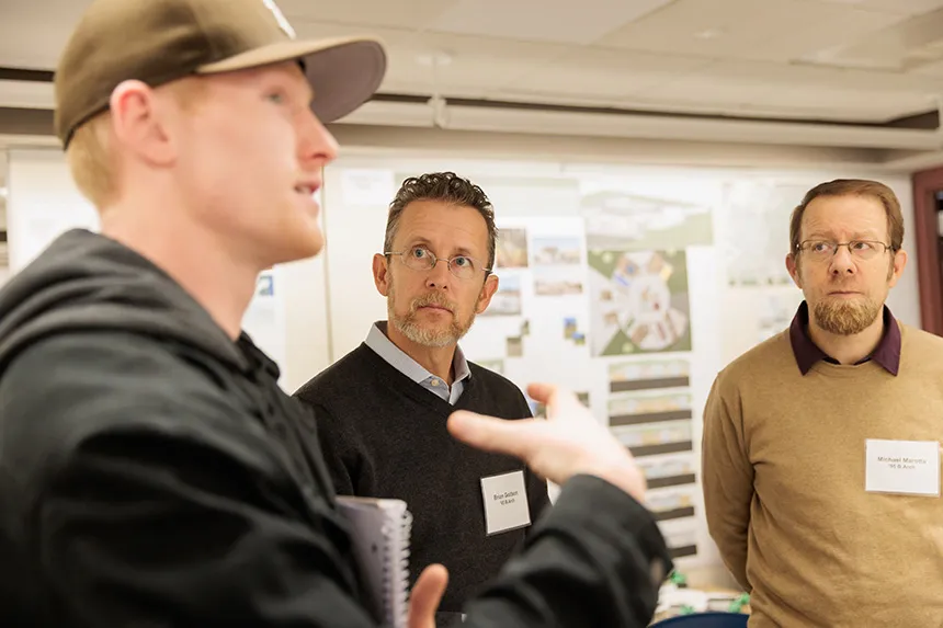 A close-up of a student and two alumni reviewers standing and talking