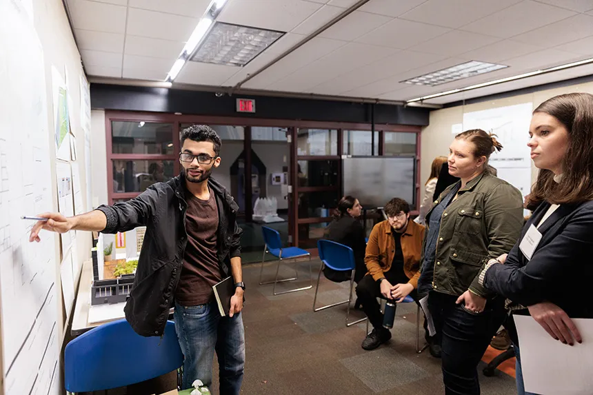 An Architecture major points to a poster design as a handful of reviewers look on