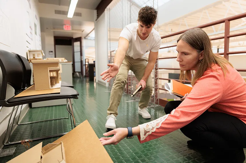 A student and a reviewer crouch down to look at a 3D design of a building