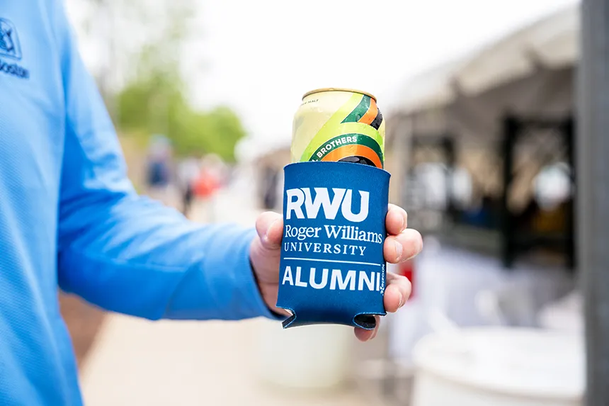 An alum enjoys a tasty beverage with a RWU-branded koozie.