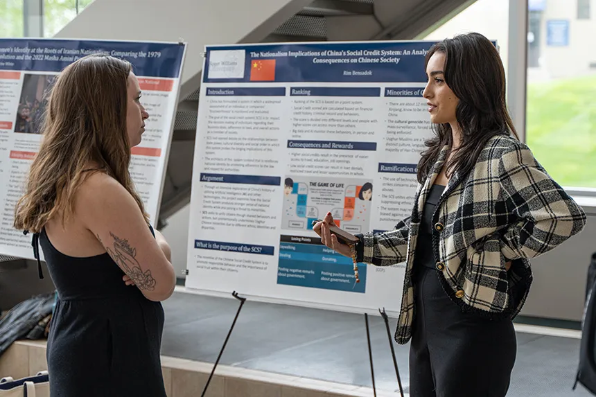 Two students, standing in front of a poster, talk at SASH. 
