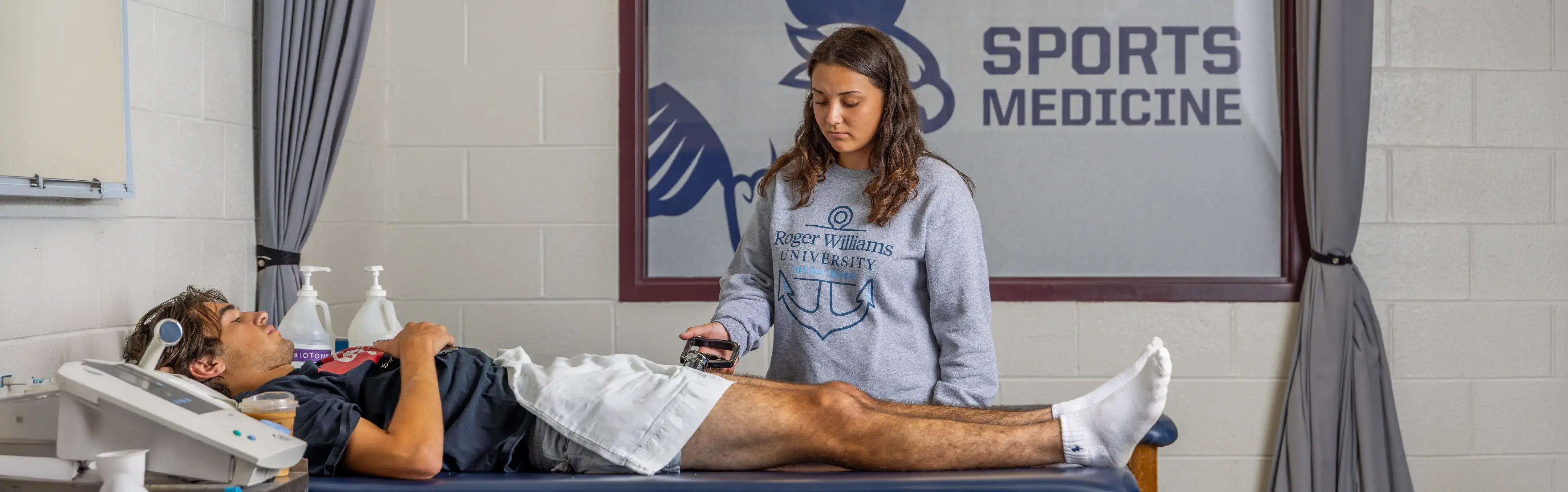 A physical therapist works on a patient with a sports medicine sign behind them.