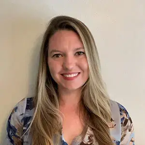 Student with long blonde hair smiles in front of a neutral background.