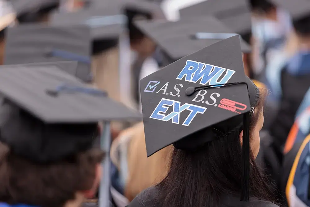 Graduate wears cap that says RWU EXT, A.S. check, B.S. loading