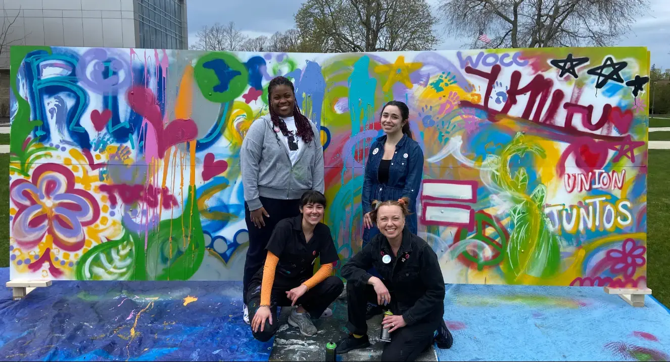 Four students posing in front of painted mural