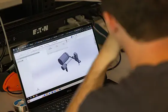 Looking over a students shoulder at a laptop with a model open that includes a cylinder and a spring